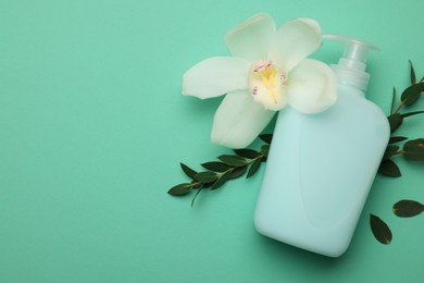 Bottle of liquid soap, eucalyptus branches and flower on turquoise background, flat lay. Space for text