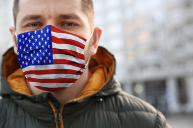 Man wearing mask with USA flag pattern outdoors, closeup. Dangerous virus