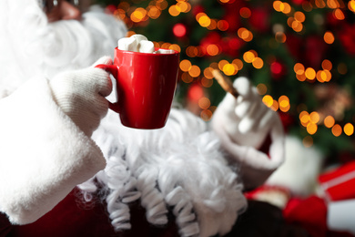 Photo of Santa Claus with hot drink and cookie against blurred Christmas lights, closeup