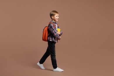 Photo of Happy schoolboy with backpack and books on brown background