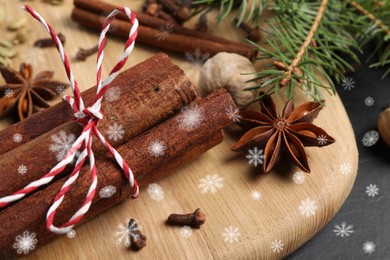 Different spices and fir tree branches on black table, closeup. Cinnamon, cloves, anise, cardamom, nutmeg