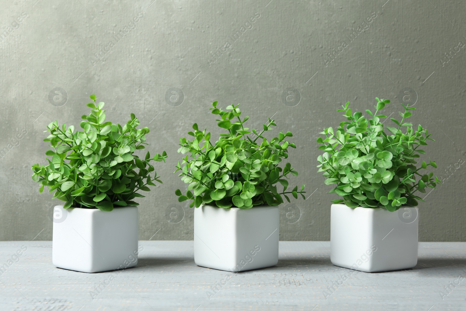 Photo of Artificial plants in white flower pots on grey wooden table