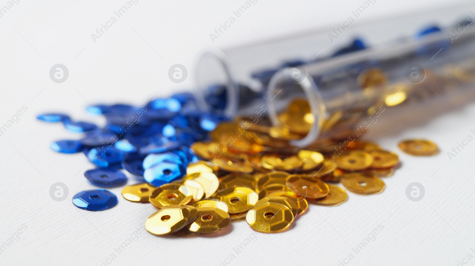 Photo of Tubes with many blue and golden sequins on white background, closeup