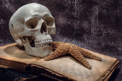 Photo of Human skull, old book and starfish on brown textured background