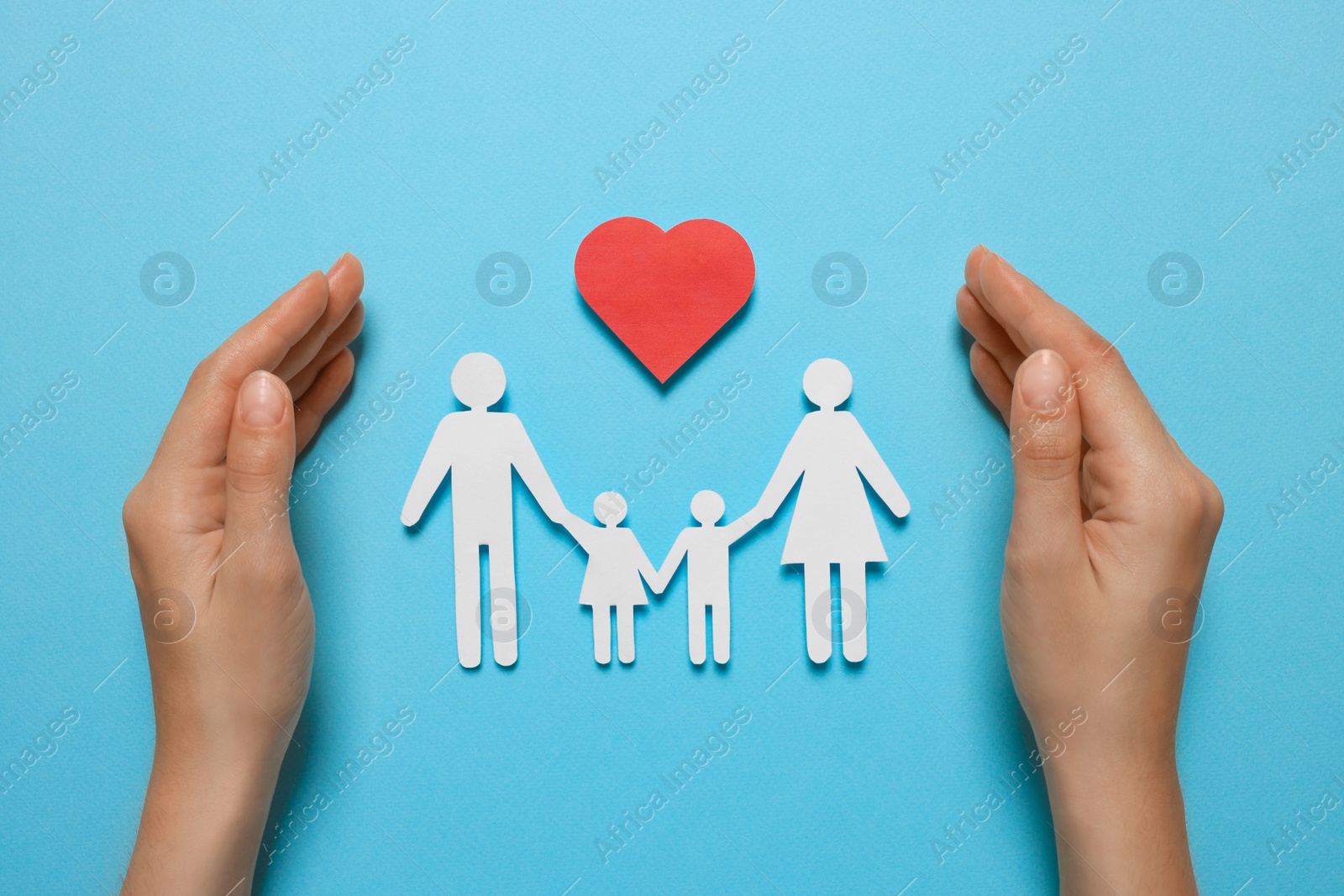 Photo of Woman protecting paper family figures and red heart on light blue background, top view. Insurance concept