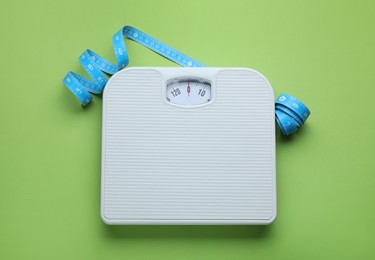 Photo of Scales and measuring tape on green background, flat lay