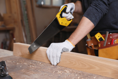 Photo of Professional carpenter sawing wooden plank in workshop, closeup