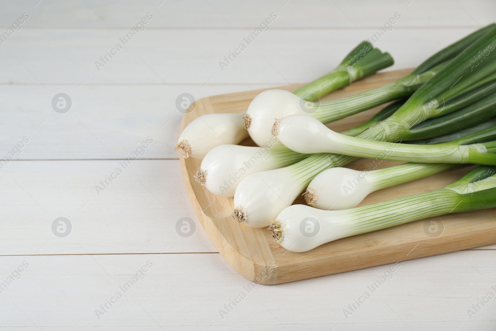 Photo of Fresh green spring onions on white wooden table, closeup. Space for text