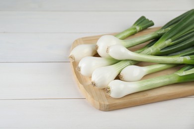 Fresh green spring onions on white wooden table, closeup. Space for text