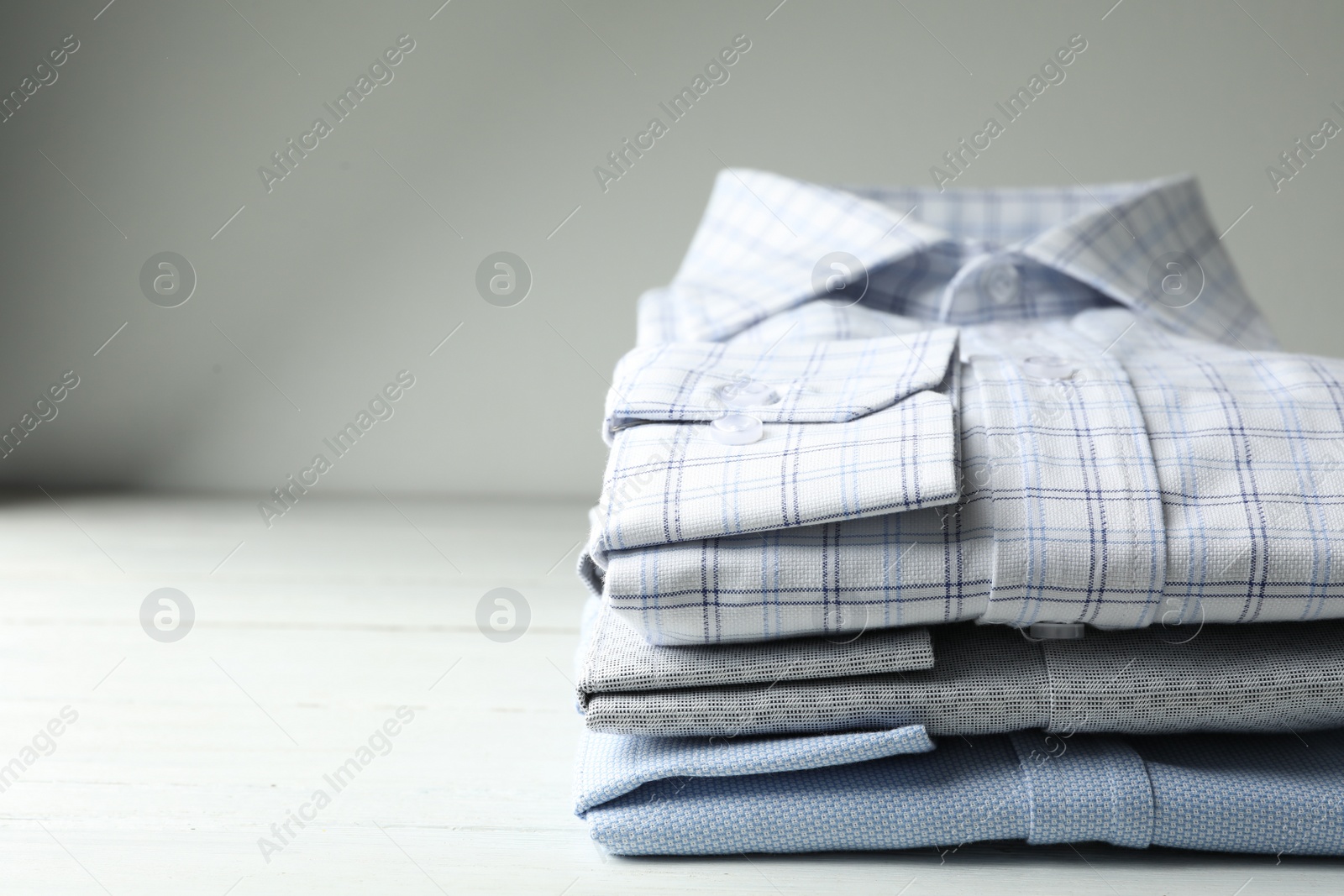 Photo of Stack of classic shirts on white wooden table. Space for text