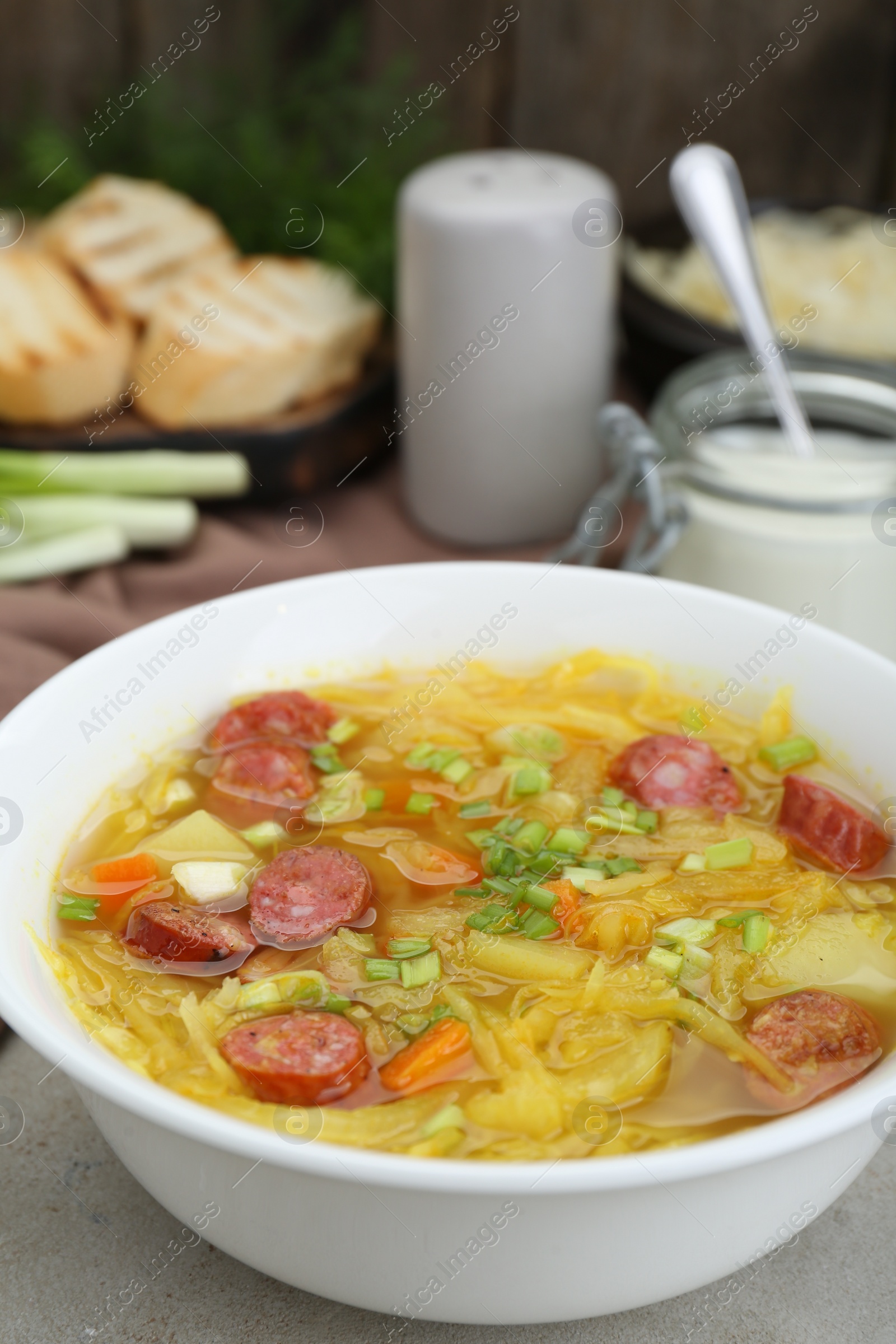 Photo of Delicious sauerkraut soup with smoked sausages and green onion on light grey table, closeup