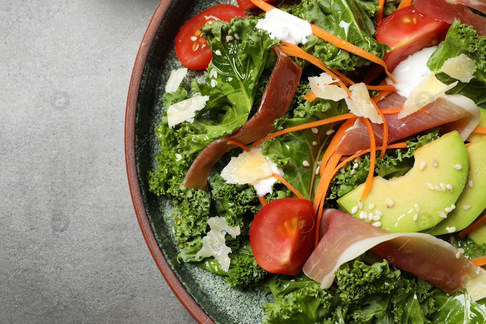 Photo of Delicious kale salad with prosciutto served on grey table, top view