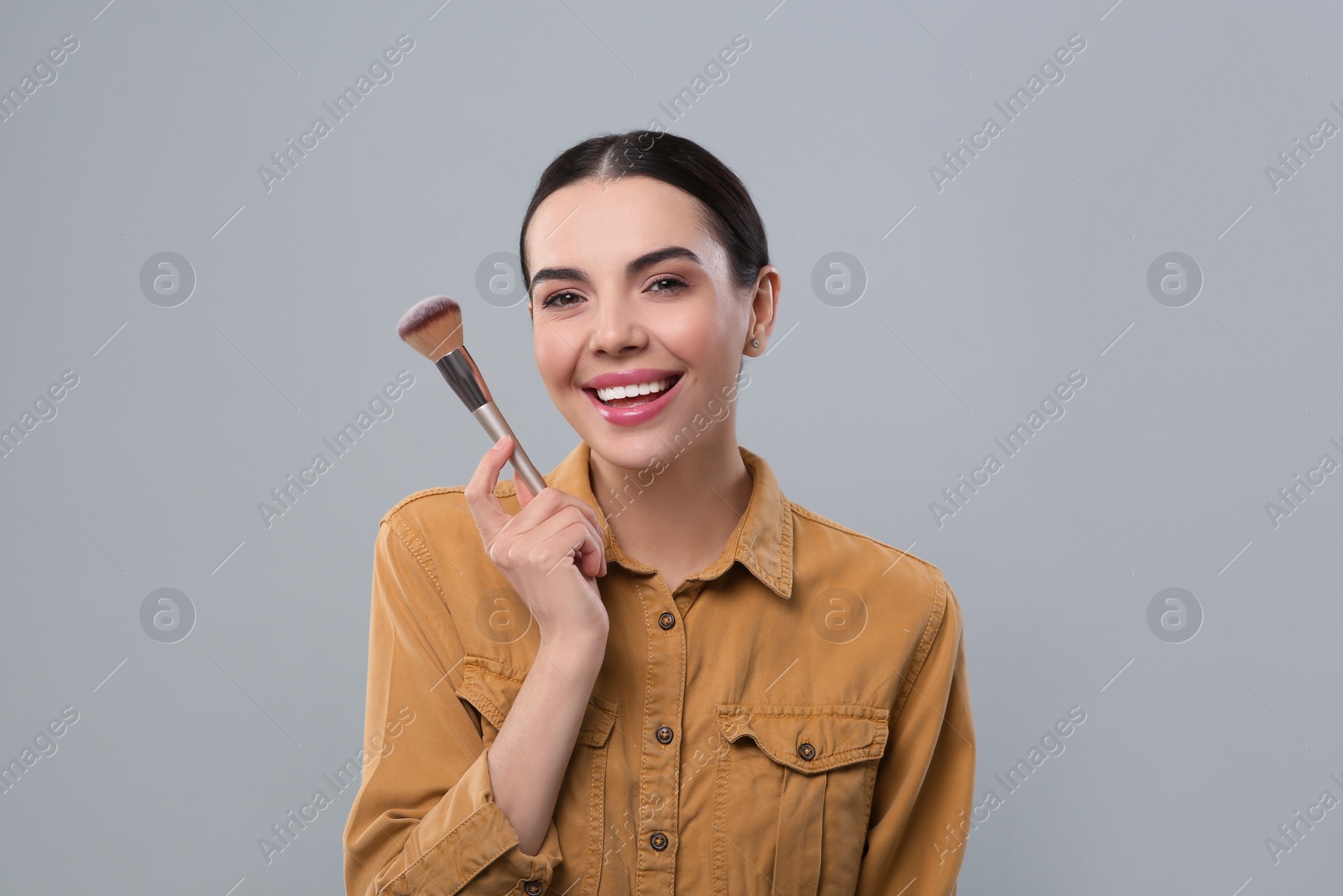 Photo of Happy woman with makeup brush on light grey background