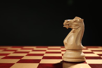 Photo of Wooden knight on chessboard against dark background, space for text