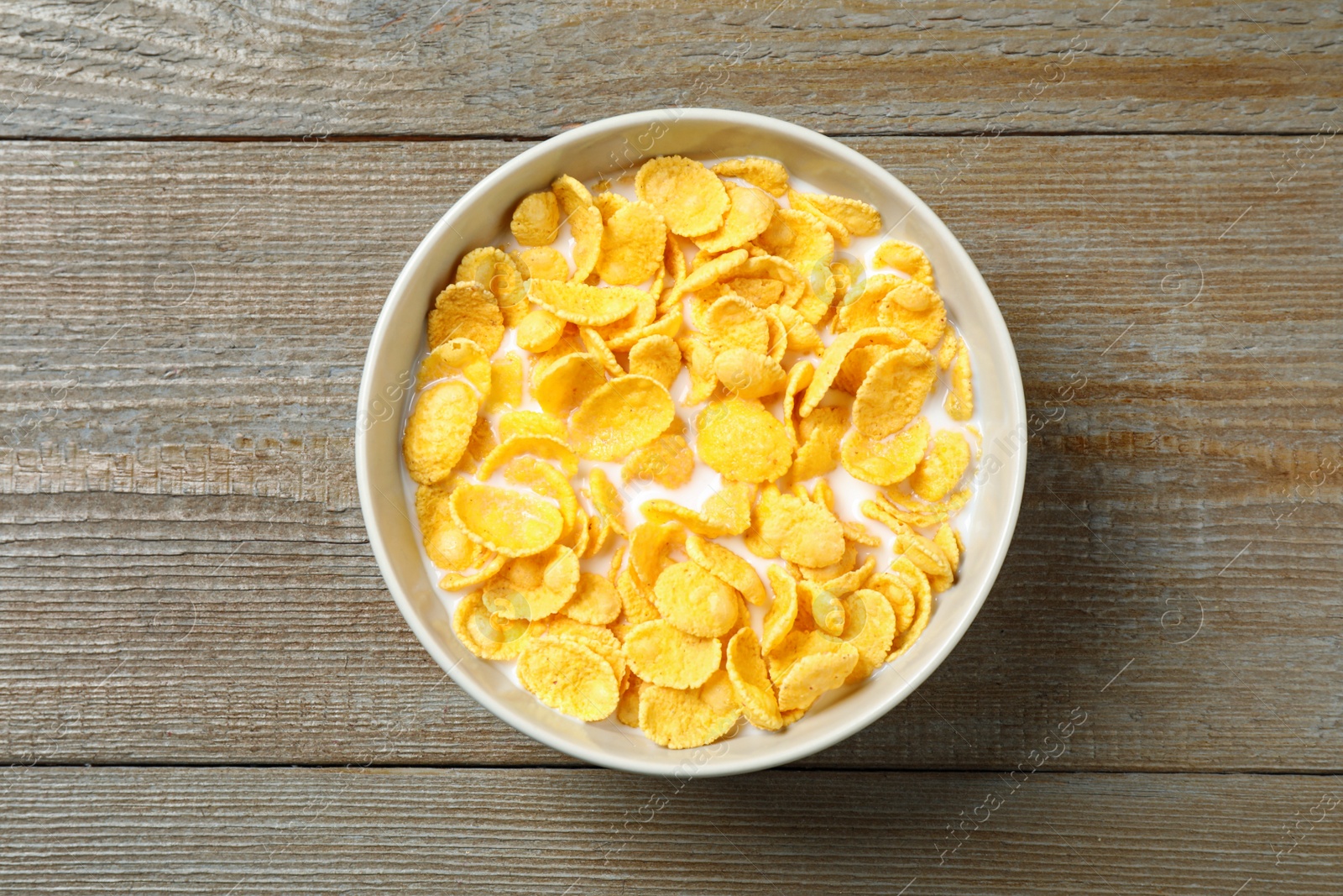 Photo of Tasty crispy corn flakes with milk on wooden  table, top view