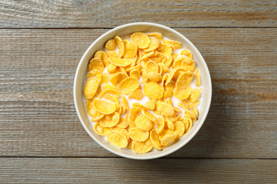 Tasty crispy corn flakes with milk on wooden  table, top view