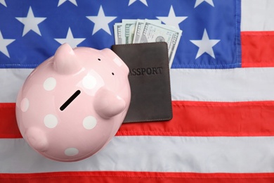 Pink piggy bank, passport and money on national USA flag, top view. Space for text