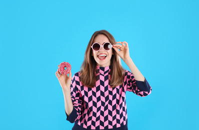 Beautiful young woman wearing sunglasses with donut on light blue background