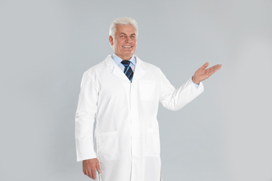 Happy senior man in lab coat on light grey background