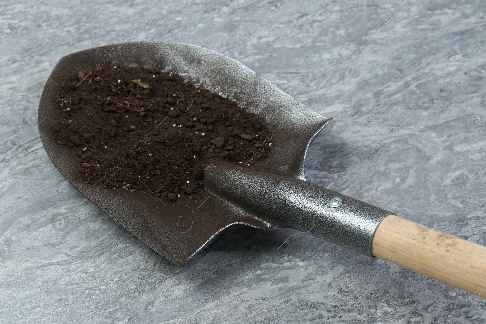 Metal shovel with fertile soil on gray textured surface, closeup Photo of Metal shovel with fertile soil on gray textured surface, closeup