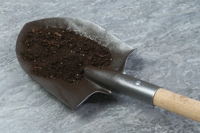Photo of Metal shovel with fertile soil on gray textured surface, closeup