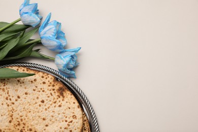 Photo of Tasty matzos and fresh tulips on light grey background, flat lay with space for text. Passover (Pesach) celebration