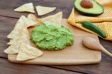 Photo of Delicious guacamole made of avocados, nachos and spoon on wooden table