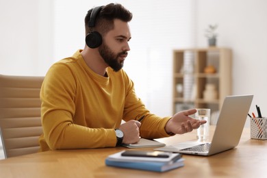 Young man in headphones using video chat during webinar at table in room