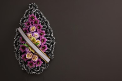 Photo of Funeral wreath of plastic flowers with ribbon hanging on dark grey wall, space for text
