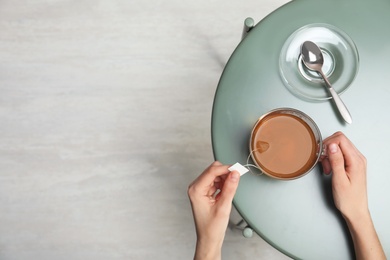 Photo of Woman brewing tea with bag in cup at table, top view. Space for text