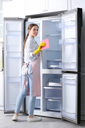 Photo of Woman in rubber gloves cleaning refrigerator at home