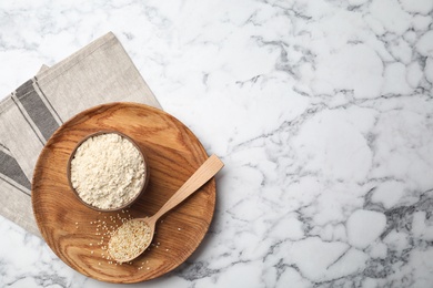 Bowl with sesame flour and seeds in spoon on marble background