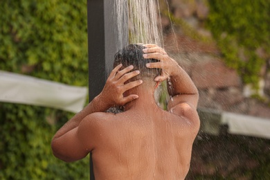 Man washing hair in outdoor shower on summer day