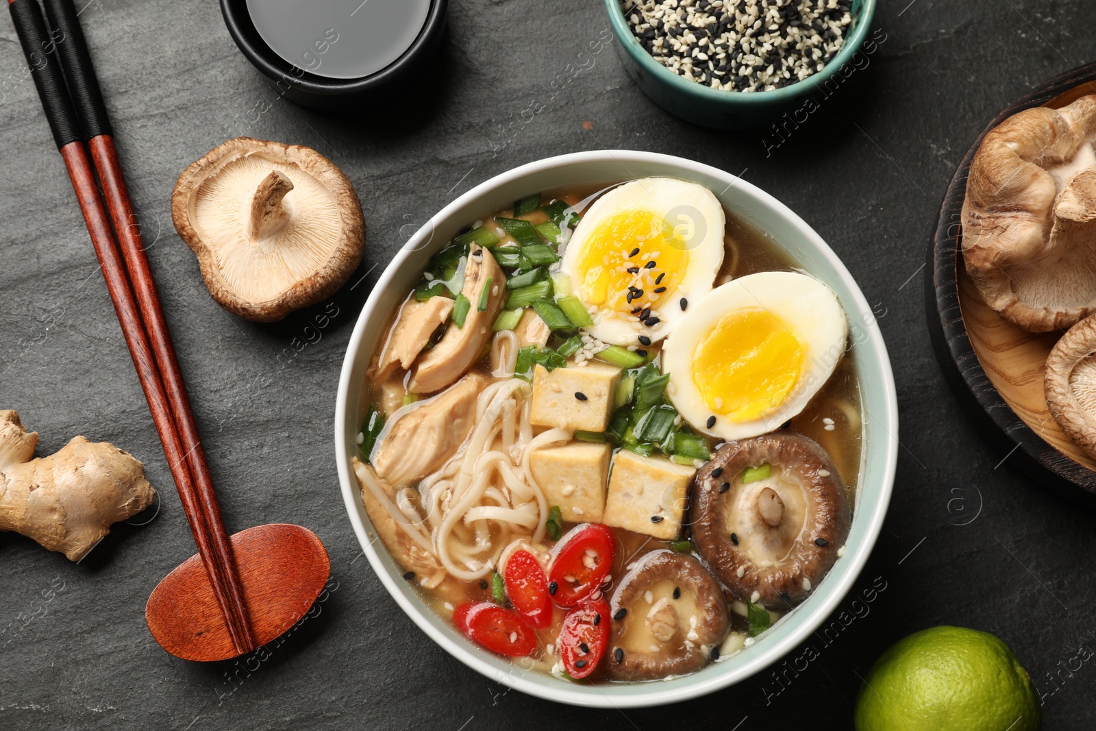 Photo of Bowl of delicious ramen, ingredients and chopsticks on black table, flat lay. Noodle soup