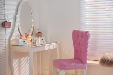 Elegant dressing table with lights and pink chair in stylish room interior