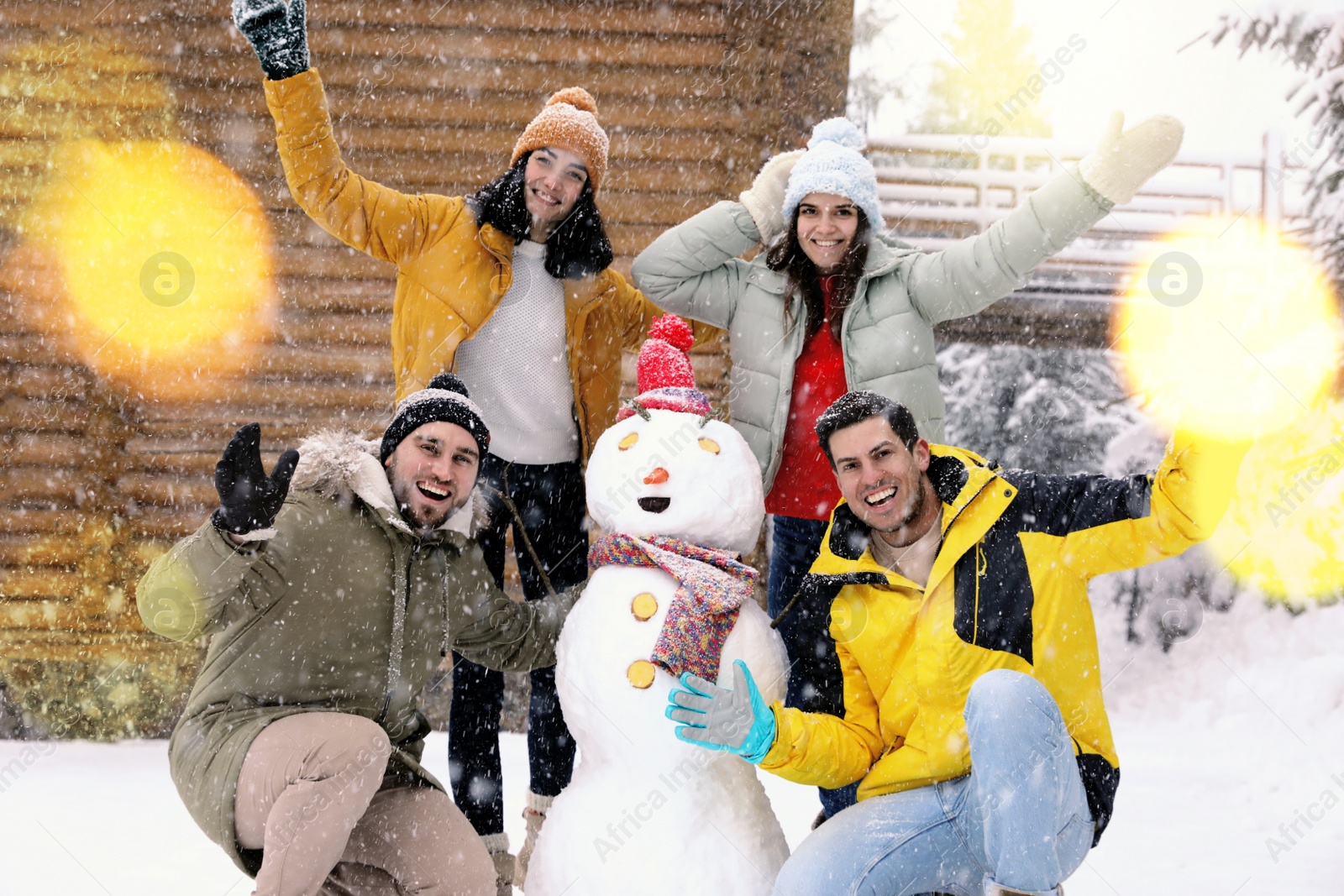 Photo of Happy friends near snowman outdoors on snowy day. Winter vacation