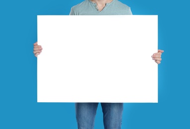Photo of Man holding blank poster on blue background, closeup