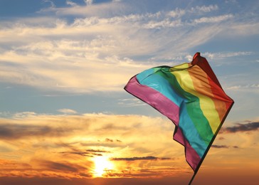 Bright rainbow LGBT flag against sky at sunset