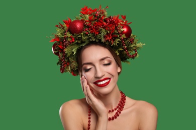 Beautiful young woman wearing Christmas wreath on green background