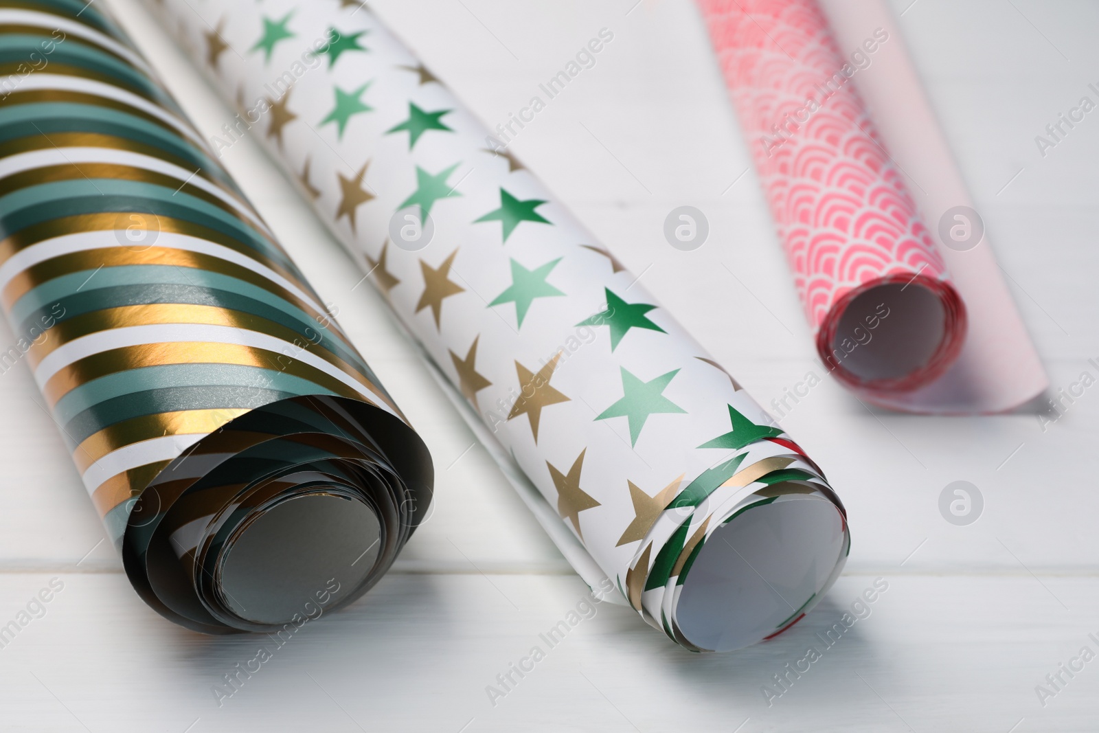 Photo of Different colorful wrapping paper rolls on white wooden table, closeup