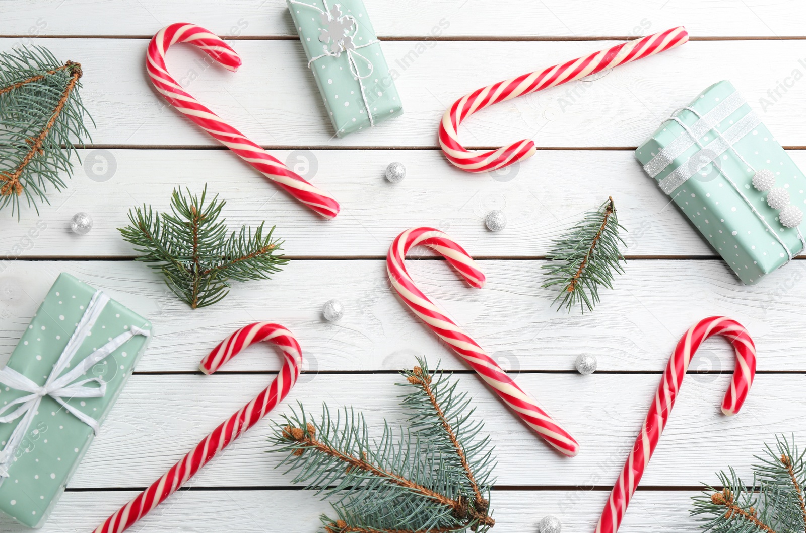 Photo of Candy canes, fir branches and Christmas gifts on white wooden table, flat lay