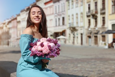 Beautiful woman with bouquet of spring flowers on city street, space for text