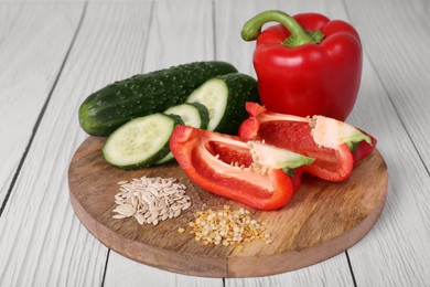 Photo of Fresh cucumbers, red bell peppers and vegetable seeds on white wooden table