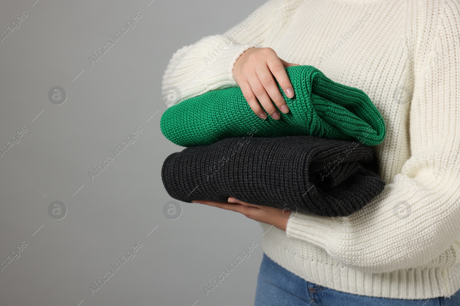 Photo of Woman with stack of knitted sweaters on grey background, closeup. Space for text