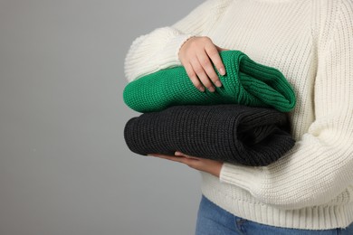 Photo of Woman with stack of knitted sweaters on grey background, closeup. Space for text