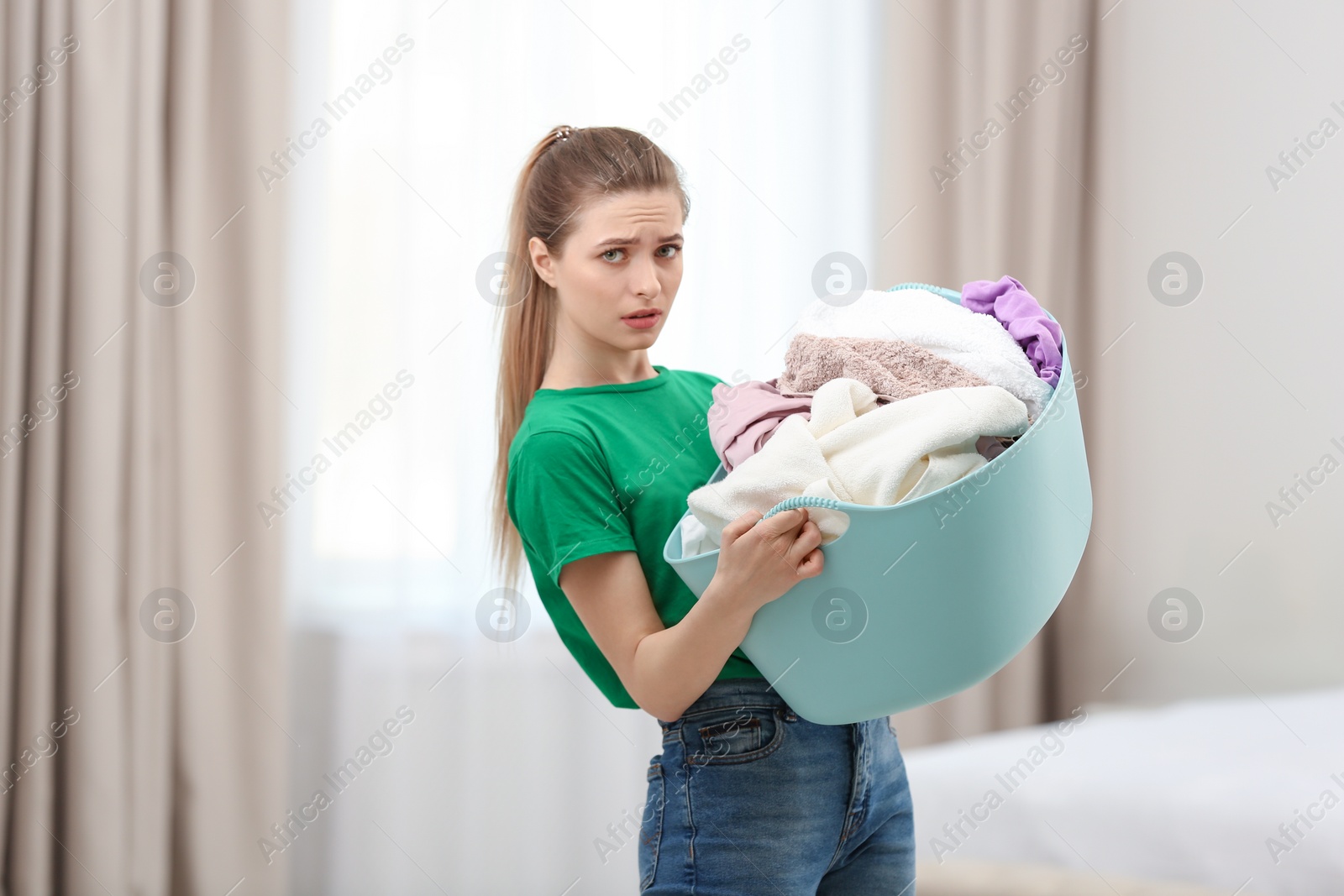 Photo of Woman holding plastic basket with dirty laundry indoors