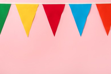 Photo of Bunting with colorful triangular flags on pink background. Space for text