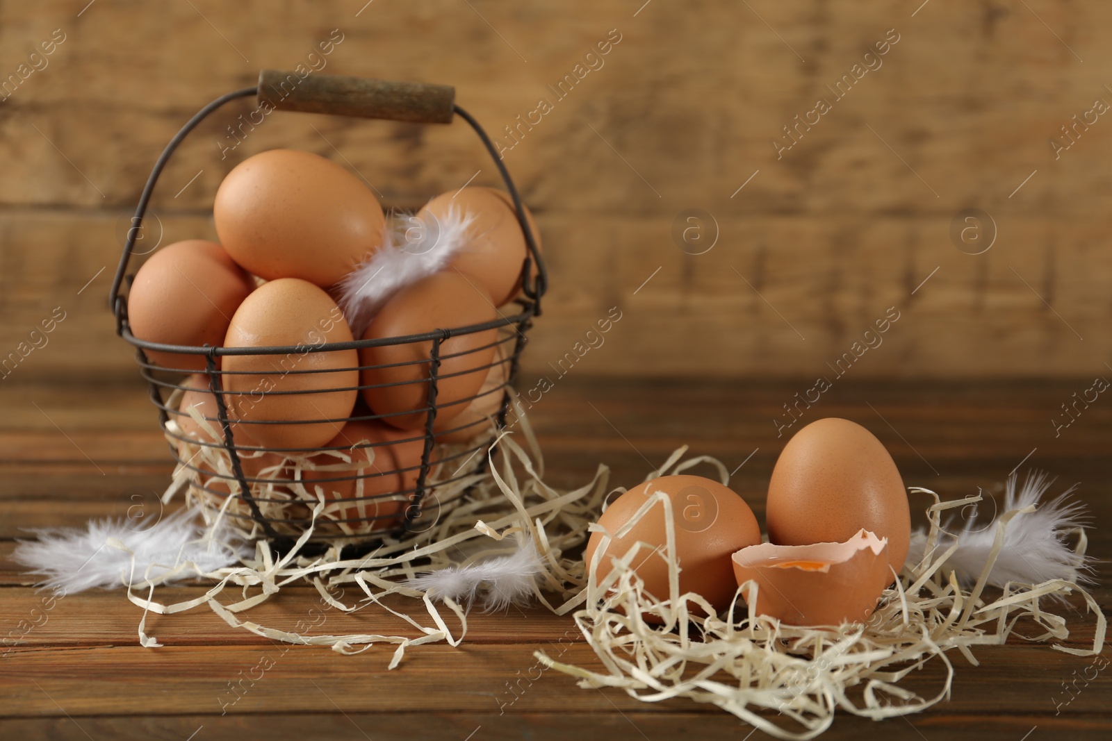 Photo of Raw chicken eggs, decorative straw and feathers on wooden table