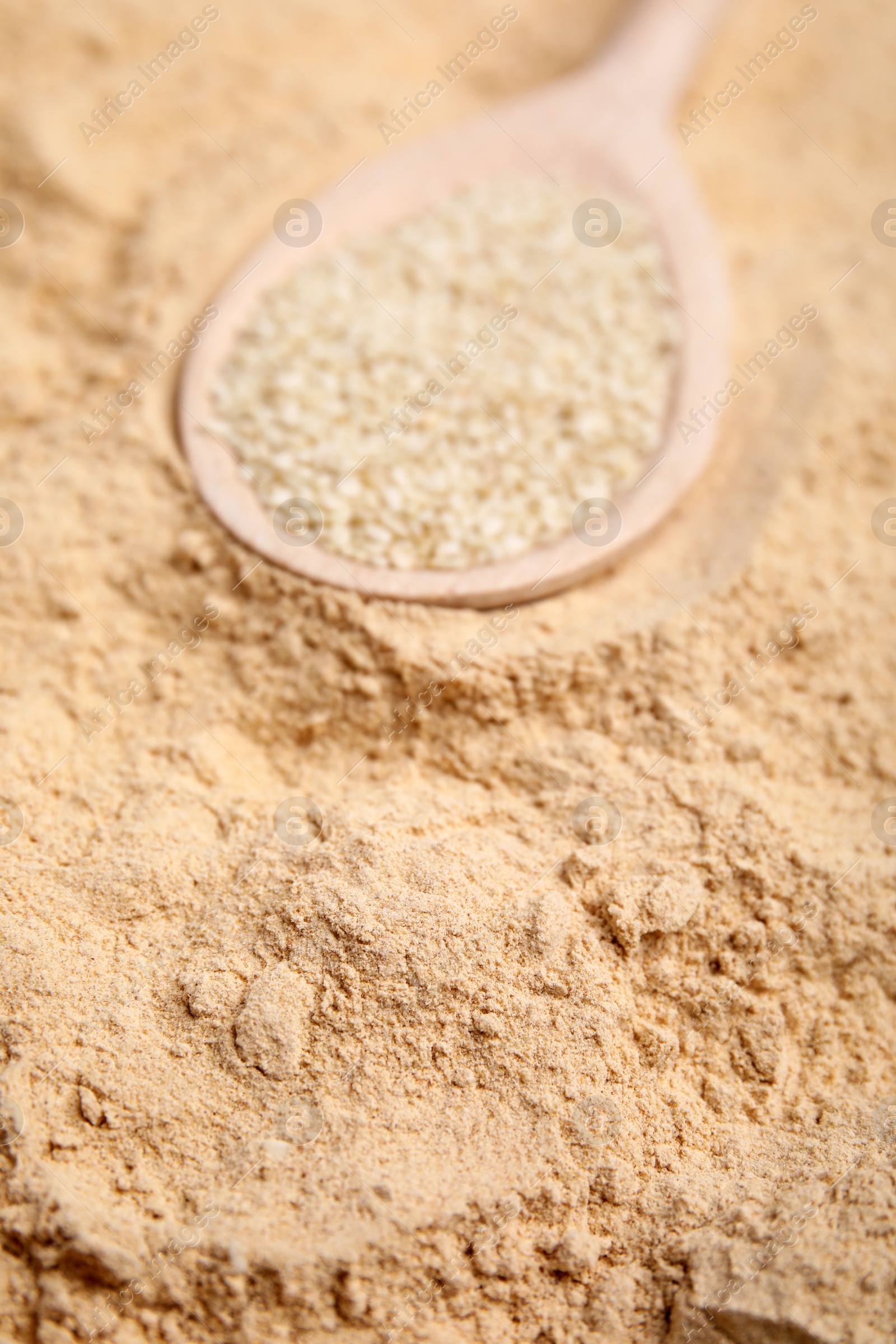 Photo of Spoon with sesame seeds on flour, closeup