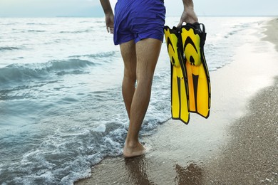 Back view of man with flippers walking on beach, closeup